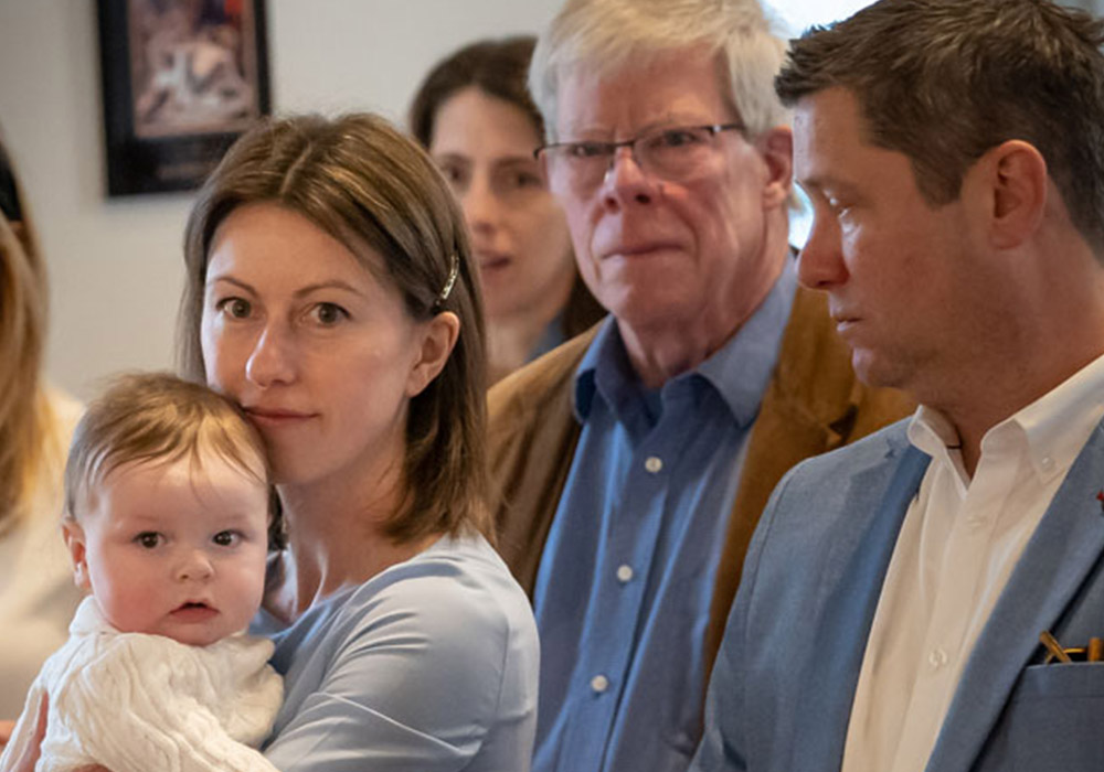 700px_media-block_0000__baptism II A family sits closely together during a church service, with a woman holding a baby in the foreground.