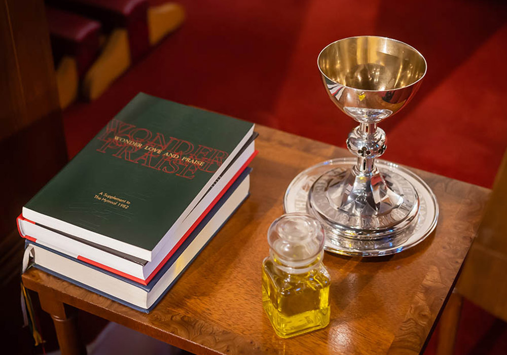 700px_media-block_0003__The Episcopal Church VII A silver chalice, glass cruet of oil, and stacked prayer books rest on a wooden table in the church.