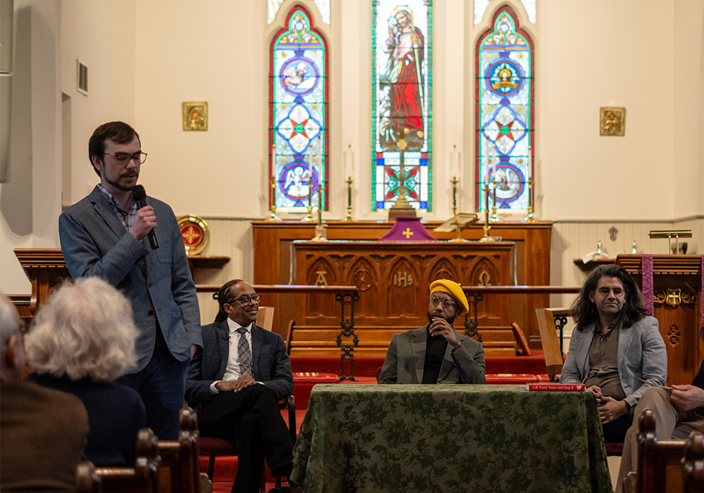 A panel discussion takes place inside the church, with speakers seated near the altar and one person standing with a microphone.
